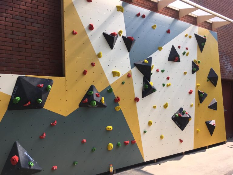 Complete climbing wall with black volumes and colourful climbing holds installed at school in Dulwich, London, UK